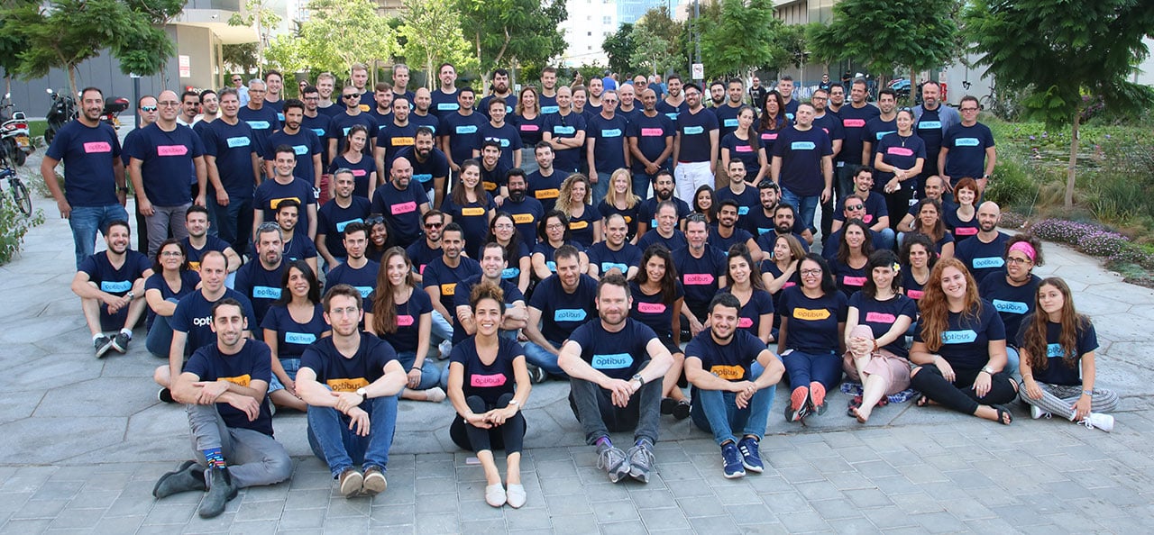 Large tech company team gathered outdoors wearing matching navy shirts with colorful name tags, posing together in a unified group photo at their urban campus location.