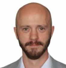 Professional headshot of a bald man with a goatee wearing a gray shirt against a neutral background, suitable for business or corporate use.