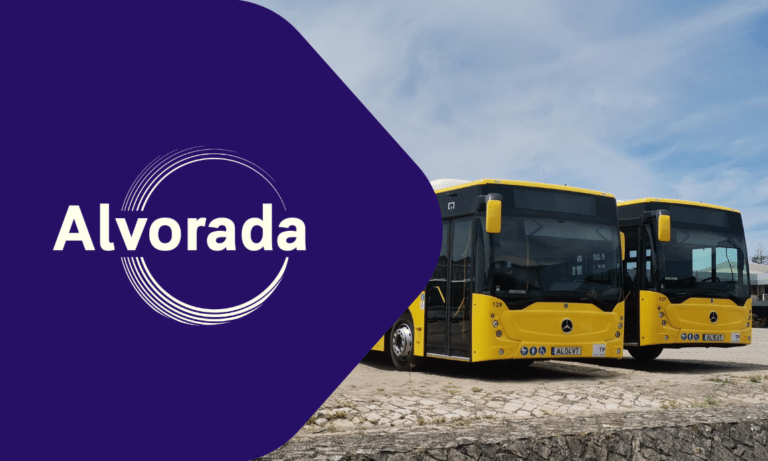 Alvorada branding displayed on a purple panel beside two yellow and black Mercedes buses parked on gravel, showcasing public transportation fleet identity.