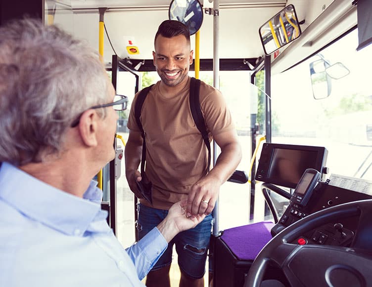 A bus driver welcomes a senior passenger aboard with a friendly handshake, demonstrating excellent customer service and community engagement in public transportation.