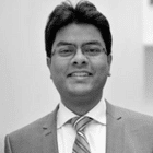 Professional headshot of a man wearing glasses and a gray suit with a striped tie, photographed in black and white against a plain background.