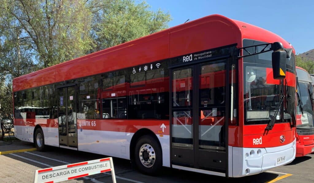 Red metropolitan bus from the Red de Movilidad transit system in Santiago, Chile, featuring modern amenities and distinctive red-and-white livery parked alongside trees.