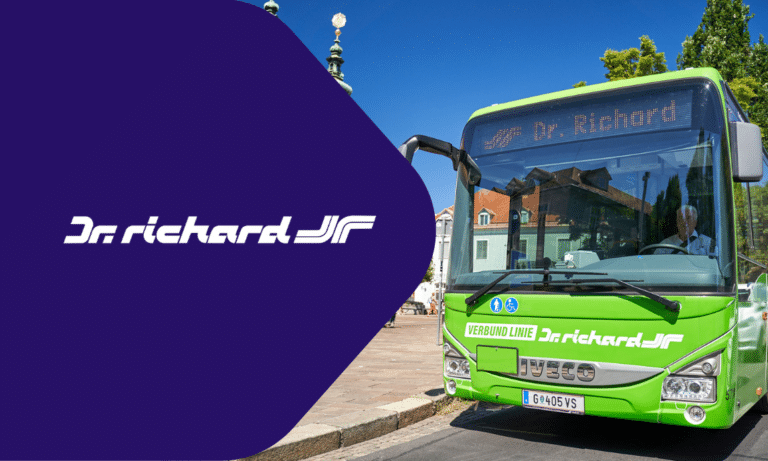 Bright green Portechard JR bus displays route information on its digital display while parked near a scenic waterfront promenade with historic architecture.