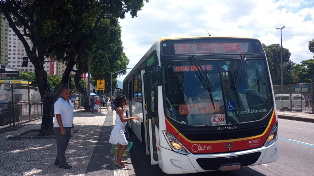 Brazilian public bus stopped at an urban station with passengers boarding, displaying route 592 Central on the digital display and air conditioning amenities.