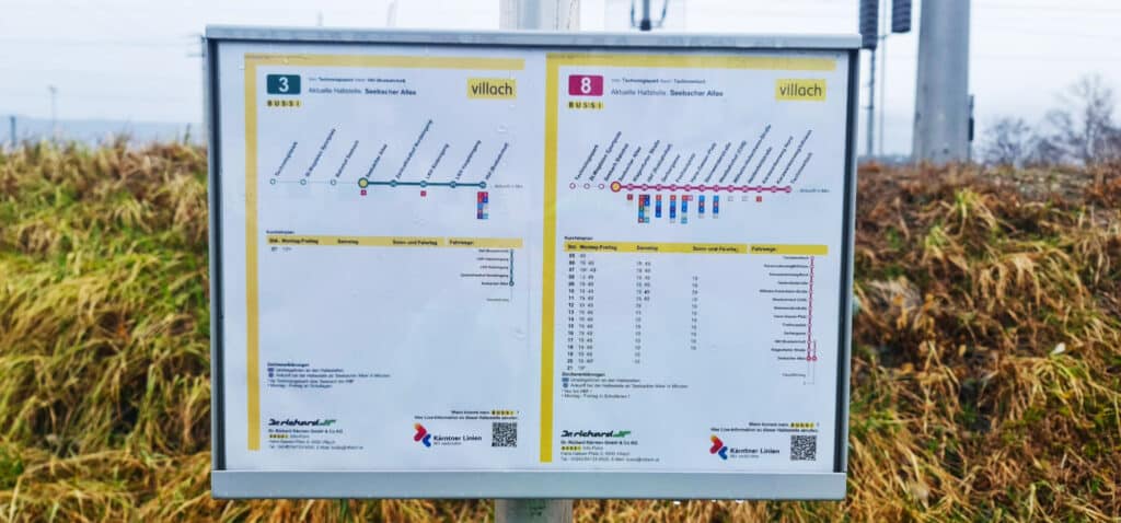 Public transit schedule signs for bus lines 3 and 8 serving Seebacher Allee in Villach, Austria, mounted outdoors with cornfields visible behind.