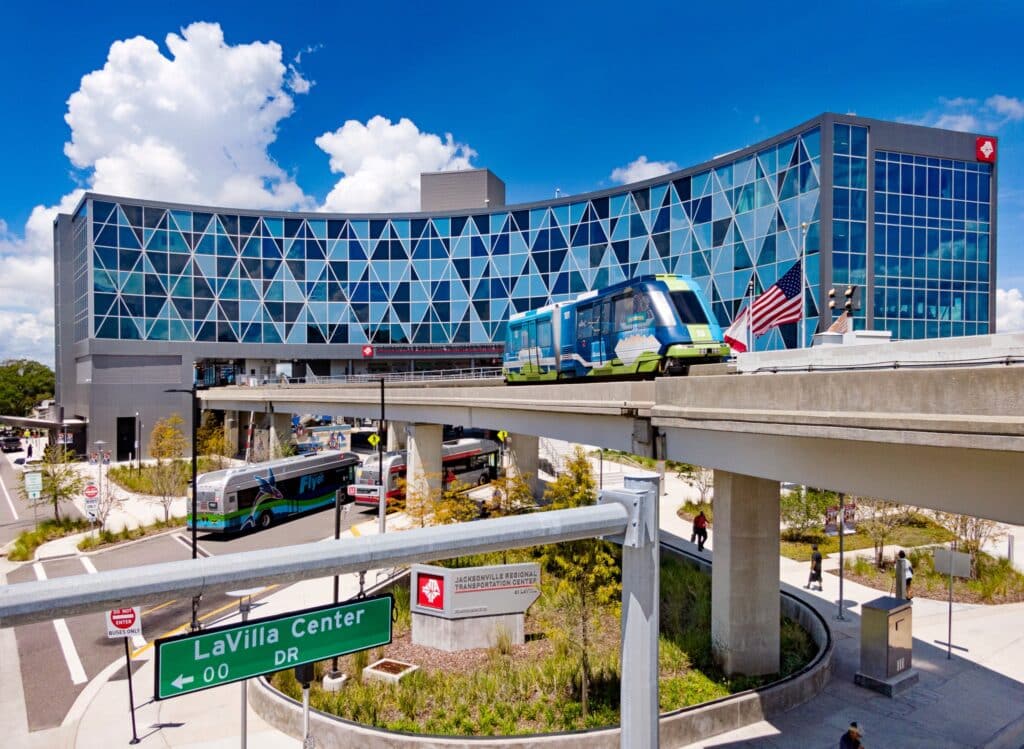 Jacksonville Regional Transportation Center with modern geometric glass facade, elevated train platform, and connected bus station below under clear blue sky.