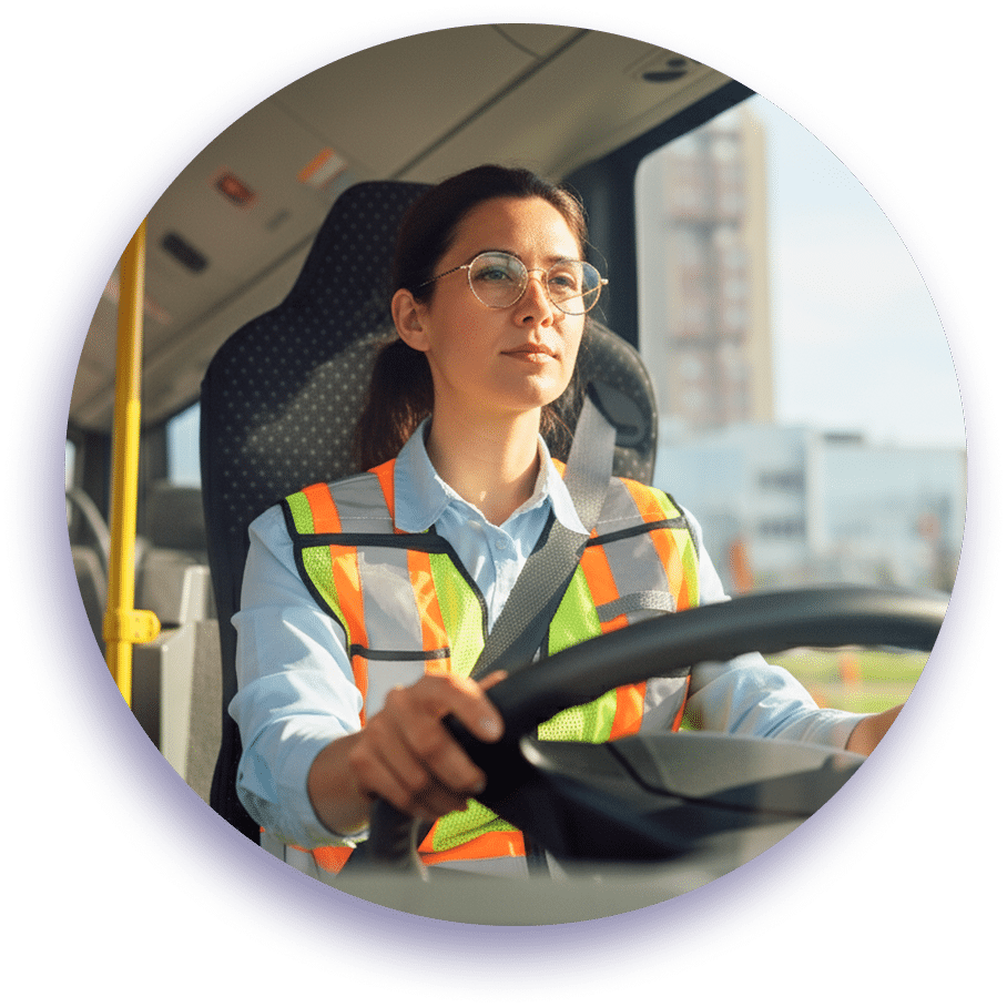 Professional female bus driver wearing safety vest and glasses operates vehicle confidently while navigating city streets during daytime commute.