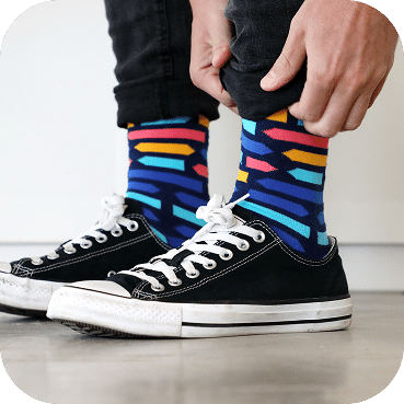 Colorful striped socks with rainbow horizontal lines pair boldly with classic black and white canvas sneakers and dark jeans.
