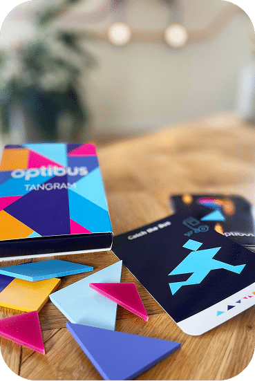 Colorful Tangram puzzle pieces arranged on a wooden table with instruction cards, featuring vibrant blue, pink, yellow, and purple geometric shapes for spatial reasoning play.