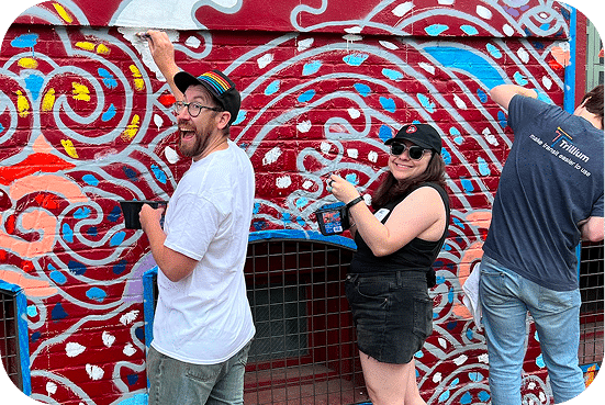 People posing and laughing in front of vibrant red street art mural featuring blue, yellow, and white abstract swirling patterns and designs.