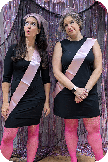 Two women wear matching black sleeveless dresses with pink sashes and bright pink tights, posing against a sparkly purple backdrop in coordinated festive outfits.