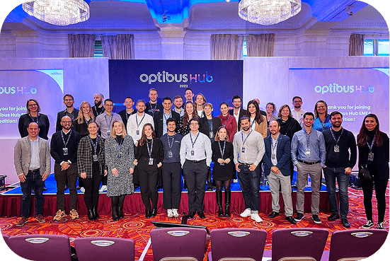 Large group of professionals posing together at an Optibus Hub conference event, standing on stage with red carpet and blue lighting in elegant ballroom setting.