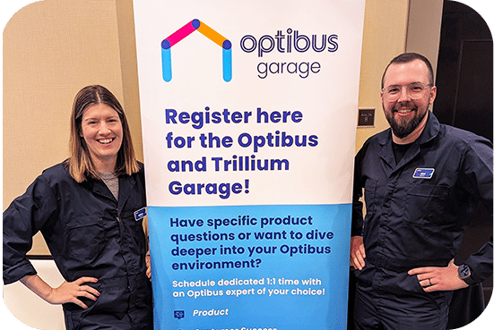 Two professionals stand beside an Optibus Garage promotional banner, encouraging registration for the Optibus and Trillium Garage event with personalized expert consultations available.