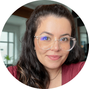 Professional headshot of a woman with long dark hair wearing clear-framed glasses and a burgundy top, smiling at the camera in an indoor setting.