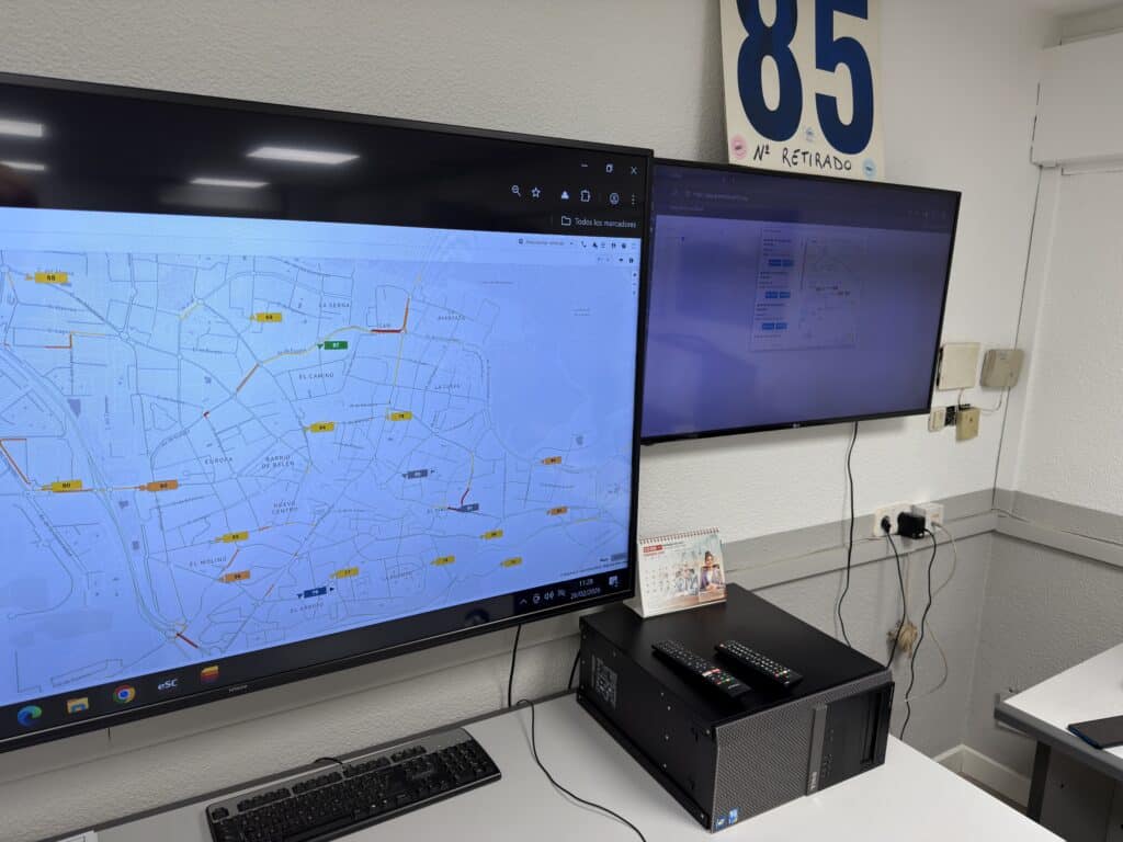 Control room setup displaying a weather map with storm tracking on the left monitor and a purple-screened interface on the right, equipped with professional monitoring equipment and dual