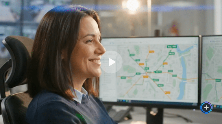 Woman in office analyzing a network map on computer monitor, showing logistics or transportation routes with green and orange location markers across a digital map interface.