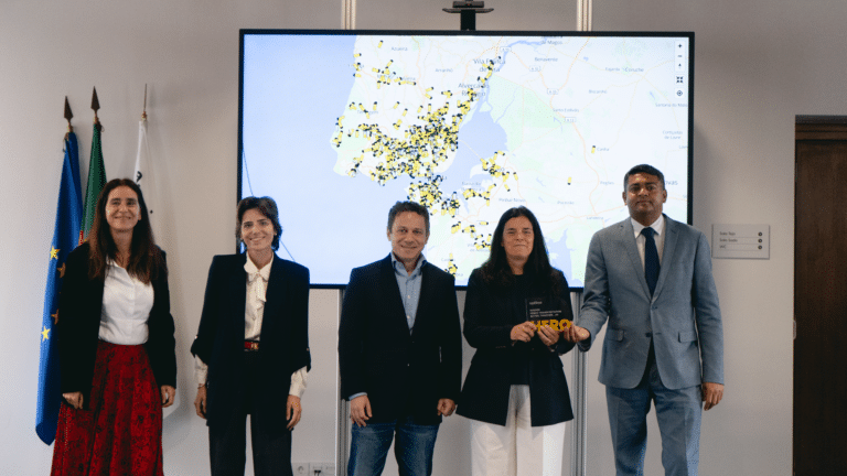 Five professionals stand before a digital map of Portugal displaying yellow and black data points. The woman in the center holds an award, flanked by colleagues at what appears to be a formal