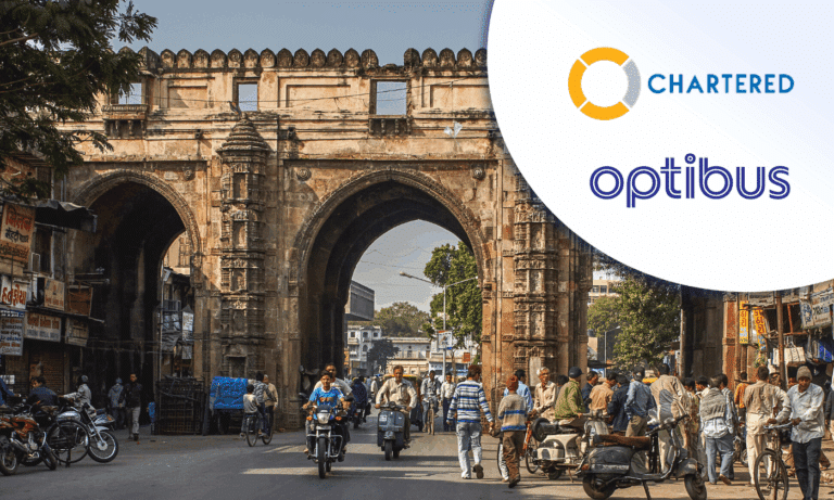 Historic stone gateway in Ahmedabad, India bustling with pedestrians, motorcycles, and bicycles beneath ornate arches decorated with detailed architectural elements and weathered stonework.