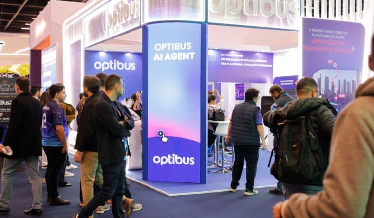 This image showcases the Optibus AI Agent booth at a trade show or industry conference. The modern blue and purple display features the Optibus branding and emphasizes their AI technology platform...